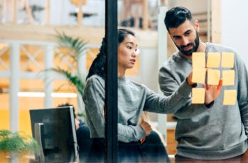 Woman and man reviewing post-it notes on interior office window.